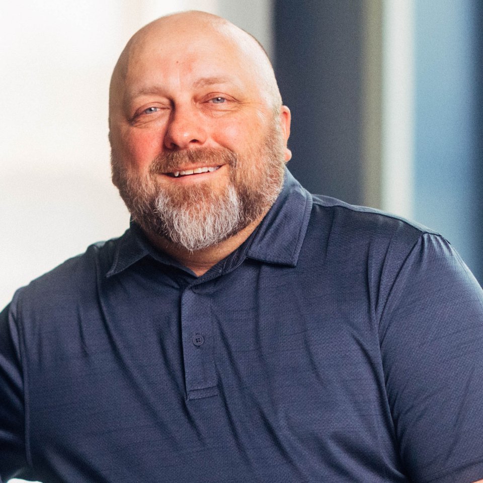 Jason Kempf smiling, wearing a navy polo, with soft window light behind him